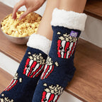 The Foozie™ Popcorn slipper socks, close-up worn on a wooden stair with a hand in a bowl of popcorn