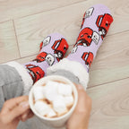 The Foozie™ Marshmallow slipper socks, worn on a wooden floor with hands holding a mug topped with marshmallows